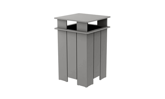 The Mainstay Trash Bin by Ledge Lounger is a tall, rectangular, gray outdoor trash can. It features a flat top and open sides with vertical slats in a modern, minimalist design. Crafted from UV stable materials, it ensures lasting durability.