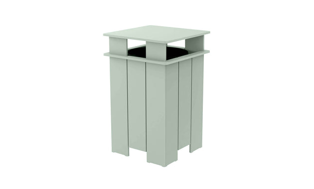 The Ledge Lounger Mainstay Trash Bin is a mint green, square outdoor patio trash can with vertical slats and a flat top. Made from UV stable materials, its open-top design features a covered structure, ideal for public spaces.