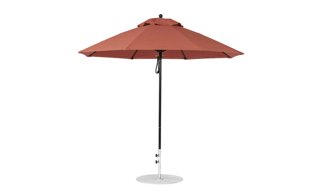 A large rust-colored Ledge Lounger Essential Fiberglass Umbrella - 9 Octagon Pulley, with a round canopy, is mounted on a black pole and silver base made from marine-grade fabrics. It stands upright against a plain white background.