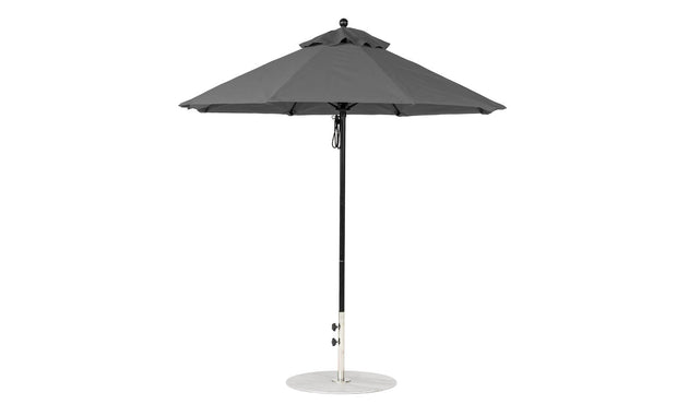 A freestanding, minimalist outdoor umbrella with a metal pole and round base is open, revealing its wide canopy. The wind-resistant Essential Fiberglass Umbrella by Ledge Lounger features marine-grade fabrics for durability and comes in a 7.5 octagon shape.