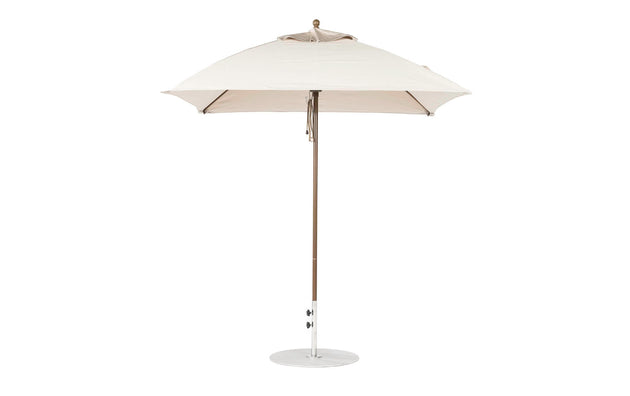 The Essential Fiberglass Umbrella by Ledge Lounger is a 7.5 square beige outdoor umbrella with a durable wooden pole and marine-grade fabrics, resting on a circular metal base, shown against a plain white background to emphasize style and durability.