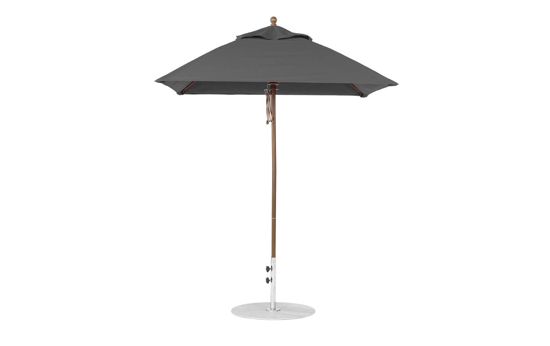 A dark gray patio umbrella by Ledge Lounger, featuring a wooden pole and round metal base, designed with marine-grade fabric. Known as the Essential Fiberglass Umbrella - 6.5 Square Pulley, it has a simple, elegant design and stands open on a flat white surface.