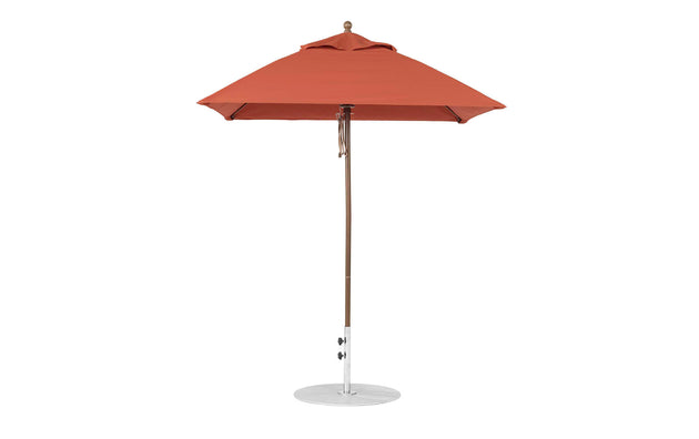 A red Essential Fiberglass Umbrella by Ledge Lounger, with a wooden pole and circular gray base, stands open. Its 6.5 square canopy is crafted from marine-grade fabrics for enhanced durability outdoors.