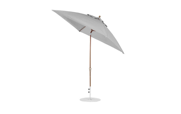 The Ledge Lounger Essential Fiberglass Umbrella, featuring a 7.5 square crank auto tilt design, has a large grey canopy made from marine-grade fabrics with a wooden pole and corrosion-resistant metal base, standing upright against a pristine white background.