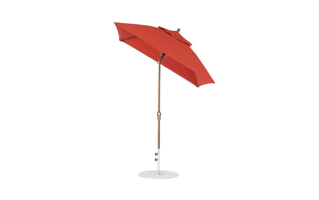 The Ledge Lounger Essential Fiberglass Umbrella, with a 6.5 square canopy and crank auto tilt feature, stands on a white circular base. Made from marine-grade fabrics, it features a corrosion-resistant wooden pole and tilts slightly to the side for style and practicality.