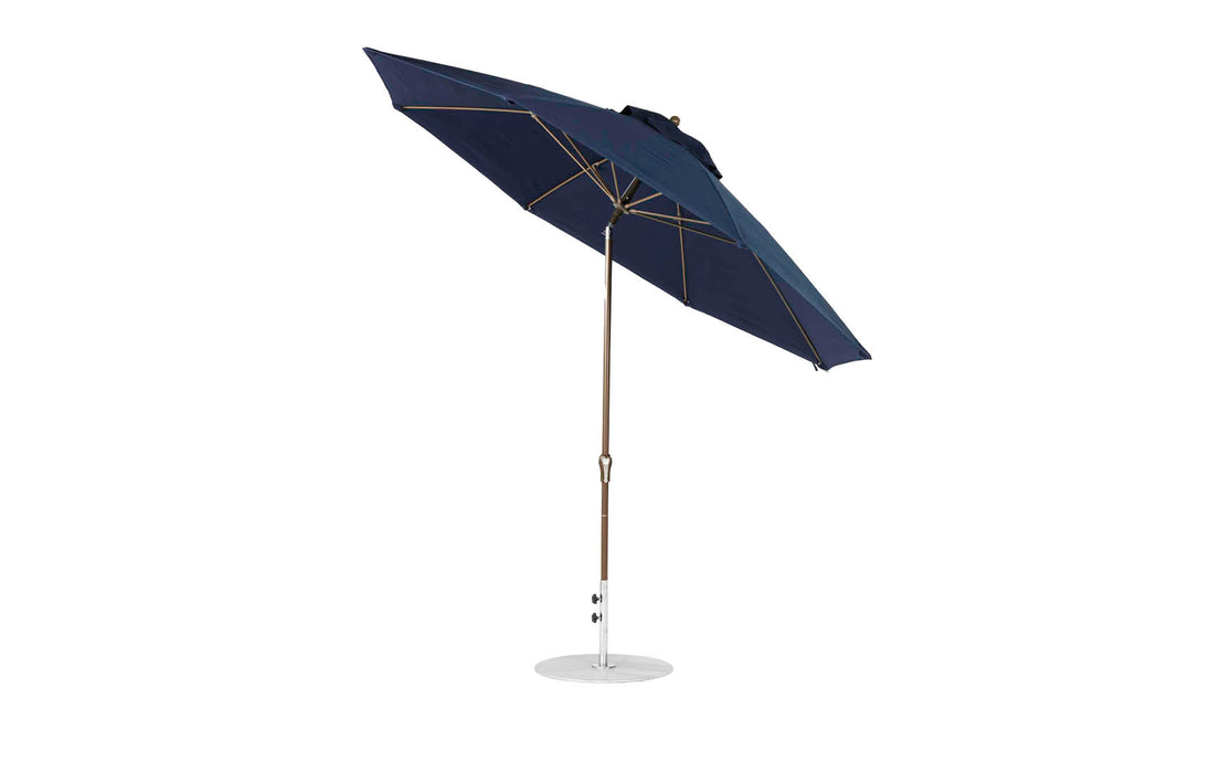 The Ledge Lounger Essential Fiberglass Umbrella boasts an 11 octagon crank auto tilt design with a dark blue marine-grade fabric canopy, a wooden pole, and white base. Its durable construction features visible metal spokes for stability.