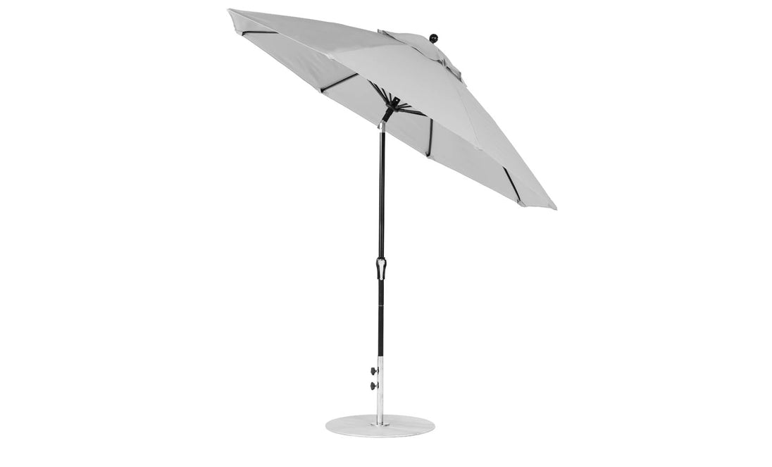 The Essential Fiberglass Umbrella - 9 Octagon Crank Auto Tilt by Ledge Lounger features a large gray marine-grade canopy, black pole, and sturdy round silver base, elegantly tilted on a white background.