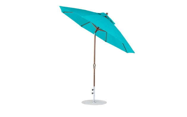 The Ledge Lounger Essential Fiberglass Umbrella - 9 Octagon Crank Auto Tilt showcases a turquoise marine-grade fabric canopy, elegantly tilted on a wooden pole with a round white base, offering both elegance and sun protection.