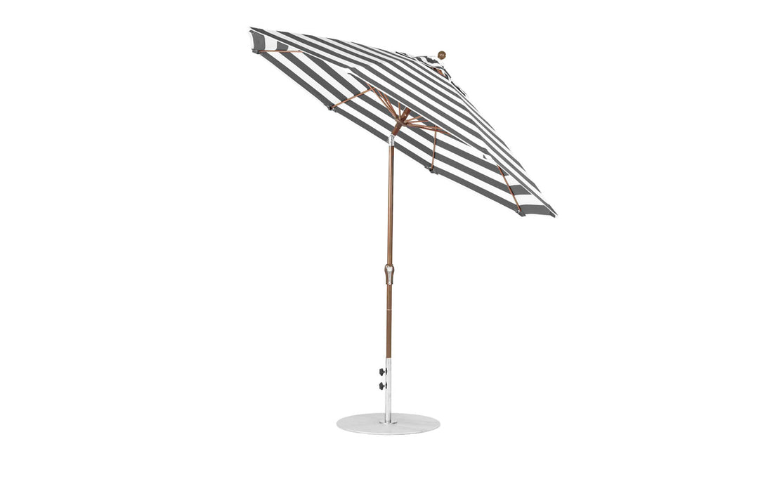 A black and white striped 9 Octagon Crank Auto Tilt Essential Fiberglass Umbrella by Ledge Lounger features a wooden pole and marine-grade fabrics. It stands open on a white circular base, tilted slightly for optimal shade.