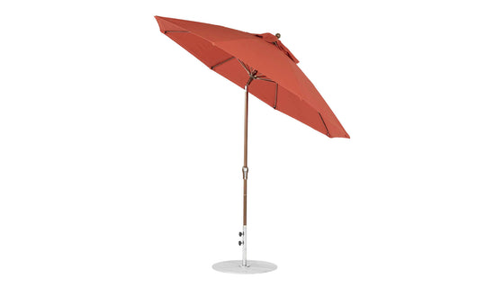 The 9 Essential Fiberglass Umbrella by Ledge Lounger, with marine-grade red fabric and a wooden pole on a white circular base, is shown fully open and slightly tilted against a plain white background.