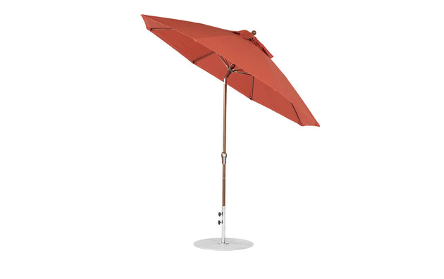 The 9 Essential Fiberglass Umbrella by Ledge Lounger, with marine-grade red fabric and a wooden pole on a white circular base, is shown fully open and slightly tilted against a plain white background.