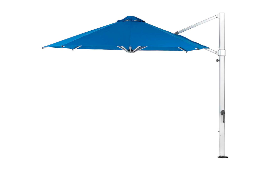 The Ultra Cantilever Umbrella - 11 Octagon from Ledge Lounger is a large, blue cantilever outdoor patio umbrella featuring an integrated rechargeable light. It opens with a robust metal stand on the side, maximizing shaded coverage without needing a central pole.