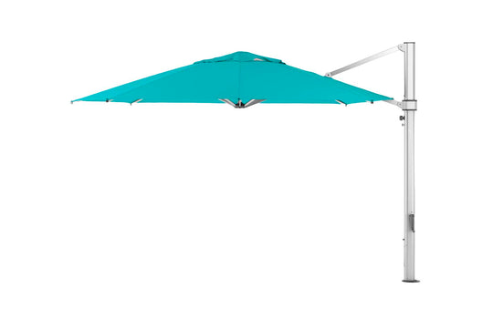 A teal Ledge Lounger Ultra Cantilever Umbrella with a silver metal stand and 13 octagon canopy, illuminated by an outdoor umbrella light. The side-positioned stand allows the canopy to extend freely for shade on your patio without a central pole.