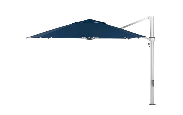 The Ultra Cantilever Umbrella by Ledge Lounger is a freestanding blue octagon umbrella with a cantilever design. It features a metal frame extending from a vertical pole, shading your patio. The canopy includes a rechargeable light for evening ambiance.