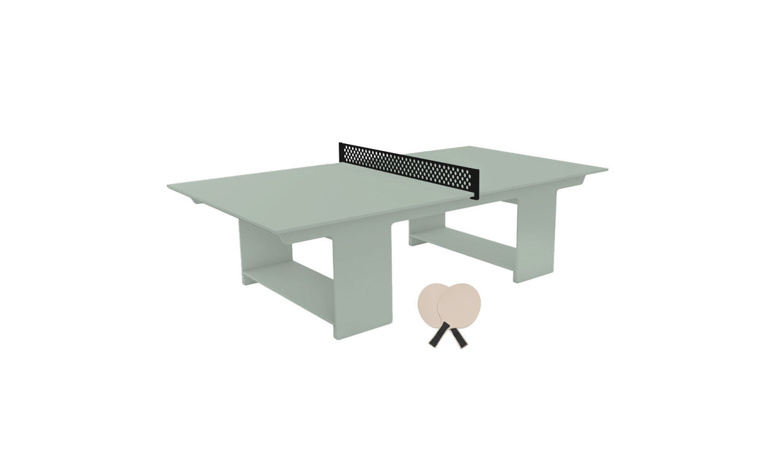 The Ledge Lounger Table Tennis Set features a light green table with a black net for outdoor fun. Two beige paddles are ready for play, and the modern block-style base adds a sleek touch to this inviting minimalist setup.