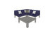 The Mainstay Sectional 4 Piece Diamond by Ledge Lounger, in navy blue, forms a cozy L-shaped corner with three white and one gray pillow. A gray coffee table sits in front of the sofa on a white background.