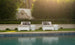 The clear poolside setting features two Ledge Loungers Affinity 2 Piece Sun Chairs in white with gray cushions. A straw hat rests on one, while tall hedges and a stone wall bask in sunlight, perfect for showcasing the UV20 rated outdoor furniture.