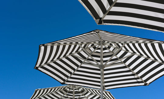 Ledge Lounger’s Signature Chaise and Side Table with Umbrella In-Pool Set features bold black and white stripes—striking geometric canopies set against a bright blue sky, perfect for enhancing your outdoor escape.