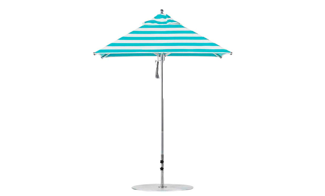 The Premier Aluminum Umbrella by Ledge Lounger features turquoise and white marine-grade fabric in a square design with a central silver pole, round base, and wind-resistant canopy that forms a conical shape. It is complemented by a small finial at the top.