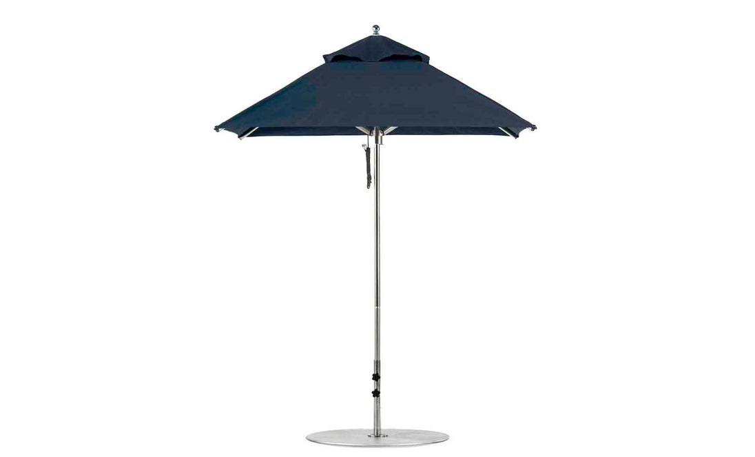 The Premier Aluminum Umbrella - 6.5 Square Pulley by Ledge Lounger is a sleek, dark blue design featuring a wind-resistant metal stand and circular base. Displayed against a white background, its wide canopy is crafted from marine-grade fabrics with a simple, modern aesthetic.