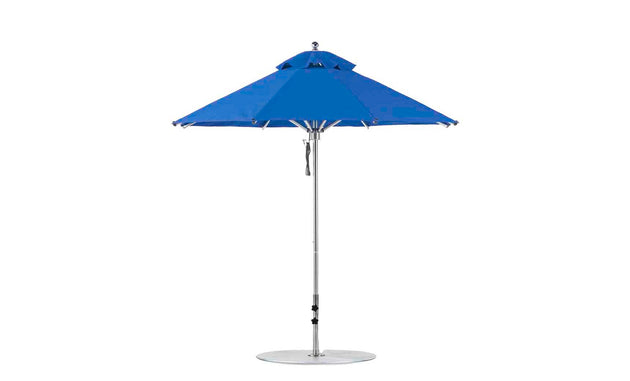 A vibrant blue Ledge Lounger Premier Aluminum Umbrella, boasting a round 7.5 octagon canopy and sleek silver pole on a flat base, is fully open, highlighting its wind-resistant design and marine-grade fabrics for durability and style.