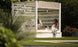 Two people relax in a durable outdoor cabana surrounded by greenery. One lounges on Ledge Loungers Shift Daybed in sunglasses, while the other, wearing a floral dress, perches on the edge, enjoying the garden view.