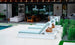 Poolside scene with three Echo Chaise loungers by Ledge Lounger, featuring light blue cushions and towels facing a shimmering swimming pool. In the background, enjoy an inviting outdoor space with comfortable sofas, a dining table, and lush greenery.