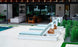 Poolside scene with three Echo Chaise loungers by Ledge Lounger, featuring light blue cushions and towels facing a shimmering swimming pool. In the background, enjoy an inviting outdoor space with comfortable sofas, a dining table, and lush greenery.