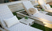 Two Ledge Lounger patterned poolside loungers with pillows sit on a lawn by the pool, one topped with a straw hat. Echo Side Tables - Final Sale, each adorned with small potted plants, are positioned between the loungers for added decor.