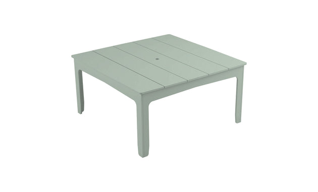 The Mainstay Square Dining Table by Ledge Lounger is a light green, plastic outdoor table with a slatted design, tapered legs, and a central hole with an umbrella sleeve, ideal for alfresco dining.
