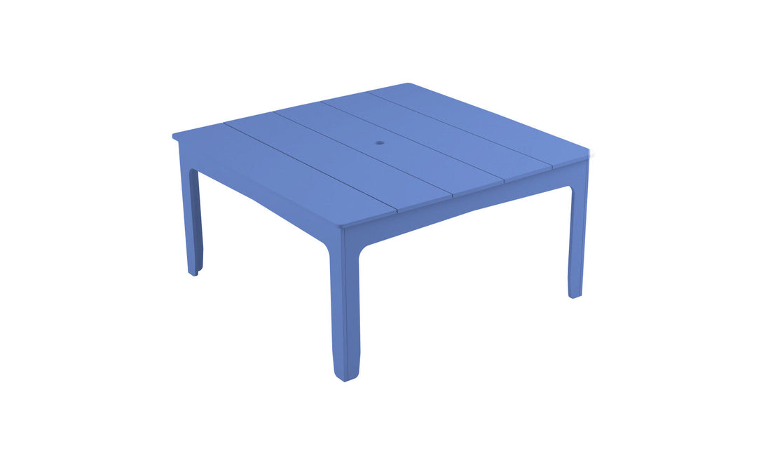 The Mainstay Square Dining Table by Ledge Lounger is a blue plastic outdoor table with clean lines, slatted tabletop, built-in umbrella sleeve, and tapered legs against a plain white background.