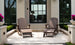 Outside a modern house with large glass doors, two Legacy Adirondack chairs and a matching Ledge Lounger Adirondack Ottoman create an inviting patio setup. The space, perfect for relaxation, features potted plants with purple blooms and trimmed greenery lining the steps.