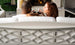A couple sits on the Legacy Sofa by Ledge Lounger, viewed from behind, holding glasses of red wine. They chat with a cozy fireplace and candles in the background, creating a relaxed atmosphere.
