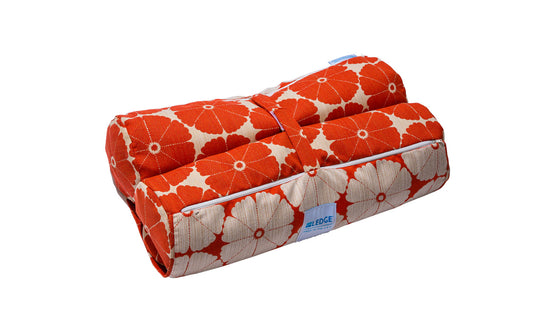 The Laze Hammock yoga mat bag from Ledge Lounger, featuring a red floral quilted design with white flowers and a blue label, is perfect for outdoor adventures. Made from marine-grade fabrics, it includes a convenient handle and rolls up securely with a strap.