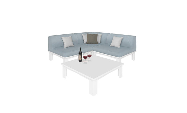 The Mainstay Sectional 4 Piece Diamond from Ledge Lounger in light blue forms a cozy corner with four cushions around a white square coffee table. The table features a wine bottle and two filled glasses, all set against a plain white background.