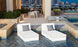 Two white Ledge Lounger chairs with gray Throw Pillow 18 Square - Final Sale pillows float in a modern rooftop pool. Nearby, theres a patio table and chairs on the deck with the city skyline visible in the background.