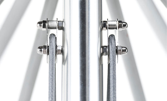 Close-up of the Essential Fiberglass Umbrella - 13 Octagon Pulley by Ledge Lounger, showcasing a central cylindrical pole with two steel cables secured by shiny metal clamps, reflecting light from the smooth surface.