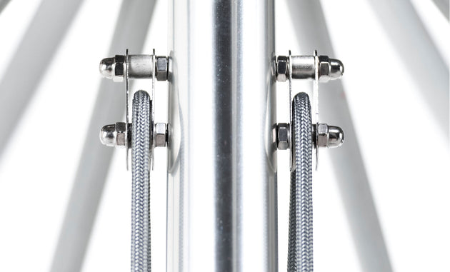 Close-up of the Essential Fiberglass Umbrella - 13 Octagon Pulley by Ledge Lounger, showcasing a central cylindrical pole with two steel cables secured by shiny metal clamps, reflecting light from the smooth surface.