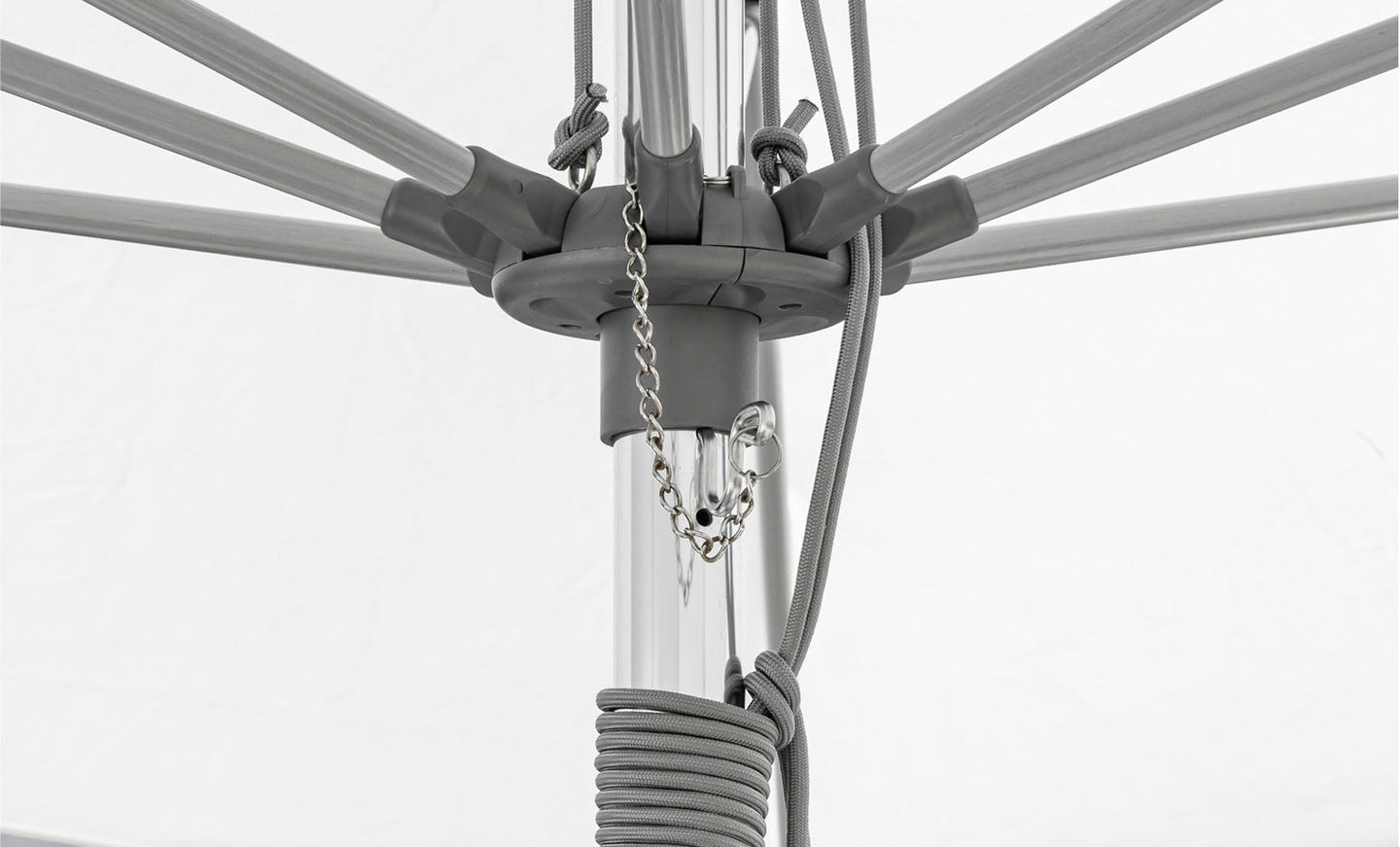 Close-up of the 10 Square Essential Fiberglass Umbrella by Ledge Lounger, highlighting its central pole with extending spokes. Chains and ropes attach to the pole, with cords wrapped around it. Marine-grade fabrics ensure durability against a white background.
