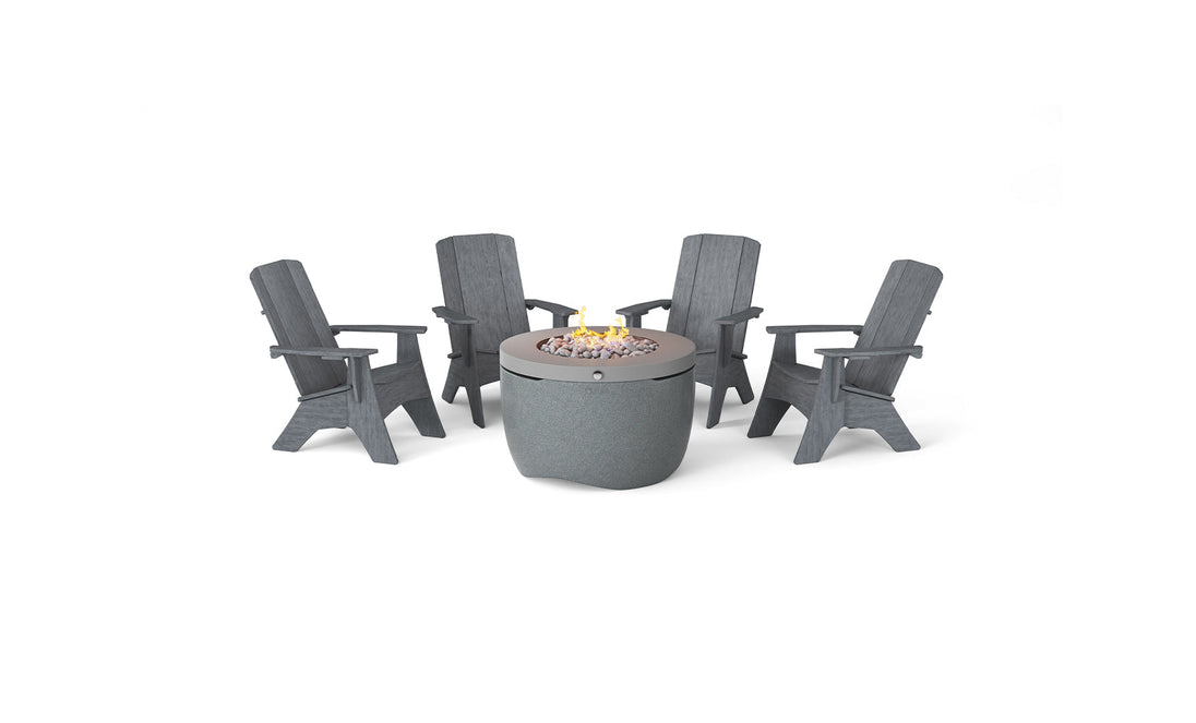 The Halo Aglow Bundle by Ledge Lounger features four dark gray Adirondack chairs around a round gray outdoor gas fire pit, embellished with small stones and a gentle central flame, set against a plain white background.
