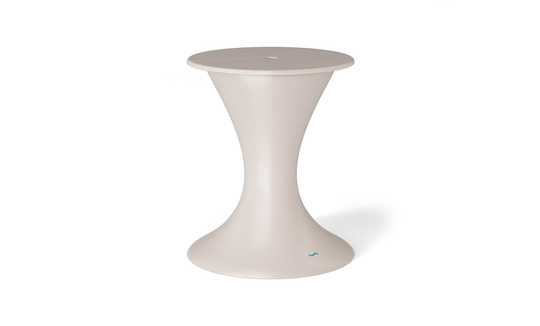 The Autograph Umbrella Stand Ice Bin by Ledge Lounger is a sleek, modern, beige hourglass-shaped stool with a smooth surface and small blue logo near the base. Ideal for outdoor gatherings, it doubles as an ice bin or serves elegantly on your patio.