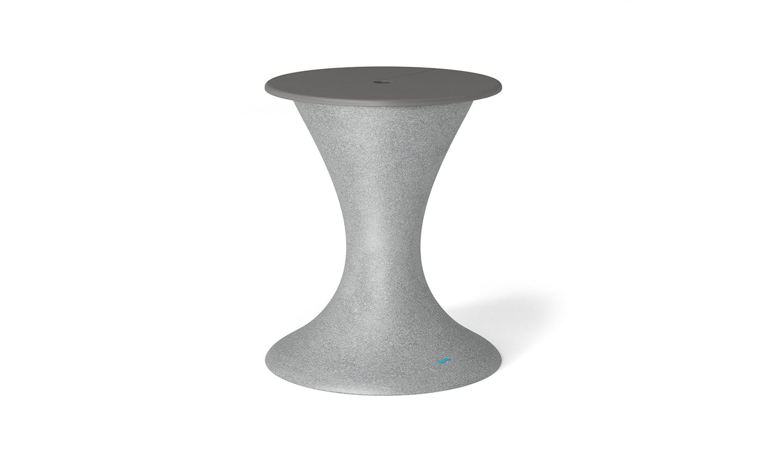 The Ledge Lounger Autograph Umbrella Stand Ice Bin is a chic hourglass-shaped outdoor table with a textured gray finish, tapering wide at the base and top. The slightly darker gray flat top has a central detail ideal for an umbrella stand.