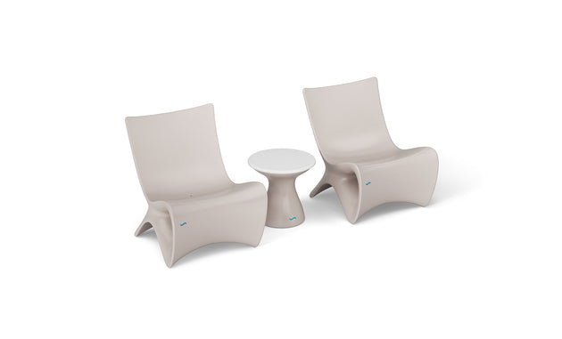 Two Classic Luxury In-Pool Chair Duo from Ledge Lounger with modern beige curves flank a small round side table with a white top. This sleek, minimalist setup is perfect for a patio or outdoor seating area.
