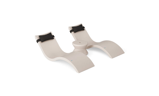 The Ledge Lounger Signature Chaise Headrest Pillow and Side Table In-Pool Set features two modern beige loungers with headrest pillows connected by a round table, creating the ideal poolside setup against a white background.