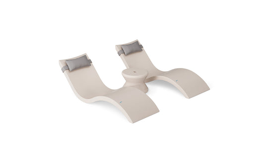 The Ledge Lounger Signature Chaise Headrest Pillow and Side Table In-Pool Set features two modern beige chaise loungers with gray headrest pillows, connected by a round center table, all styled for poolside chic against a white background.