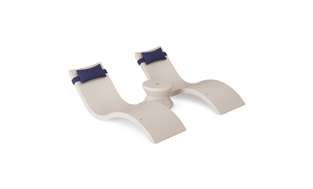 The Ledge Lounger Signature Chaise Headrest Pillow and Side Table In-Pool Set features two modern beige chaises with navy headrests, joined by a round table, all displayed against a white background.