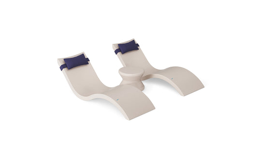 The Ledge Lounger Signature Chaise Headrest Pillow and Side Table In-Pool Set features two modern curved beige loungers with blue headrest pillows, connected by a round side table, creating a stylish poolside seating arrangement.
