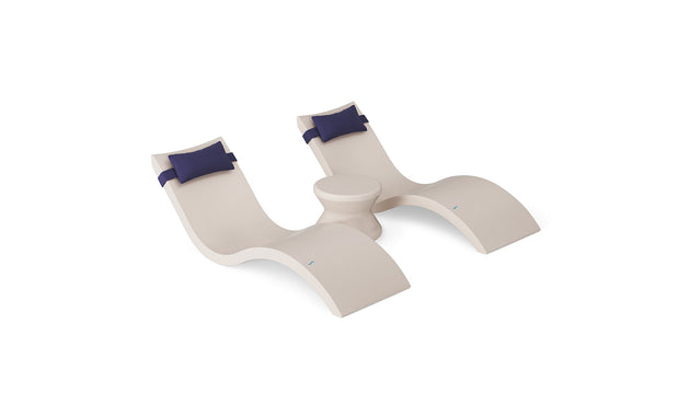 The Ledge Lounger Signature Chaise Headrest Pillow and Side Table In-Pool Set features two modern curved beige loungers with blue headrest pillows, connected by a round side table, creating a stylish poolside seating arrangement.