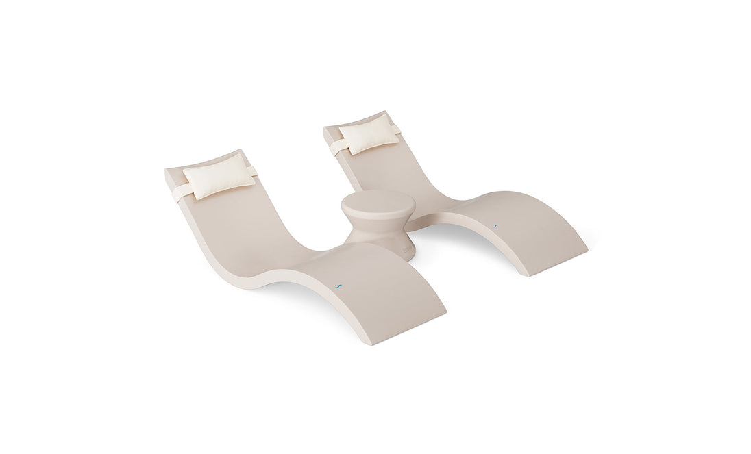 The Ledge Lounger Signature Chaise Headrest Pillow and Side Table In-Pool Set features two modern beige loungers with headrests and a round table, creating a stylish outdoor retreat perfect for relaxing poolside on a plain white background.