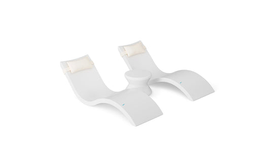 The Ledge Lounger Signature Chaise Headrest Pillow and Side Table In-Pool Set offers two modern white loungers with cream headrest pillows, connected by a round table—perfect for poolside relaxation against a sleek white backdrop.